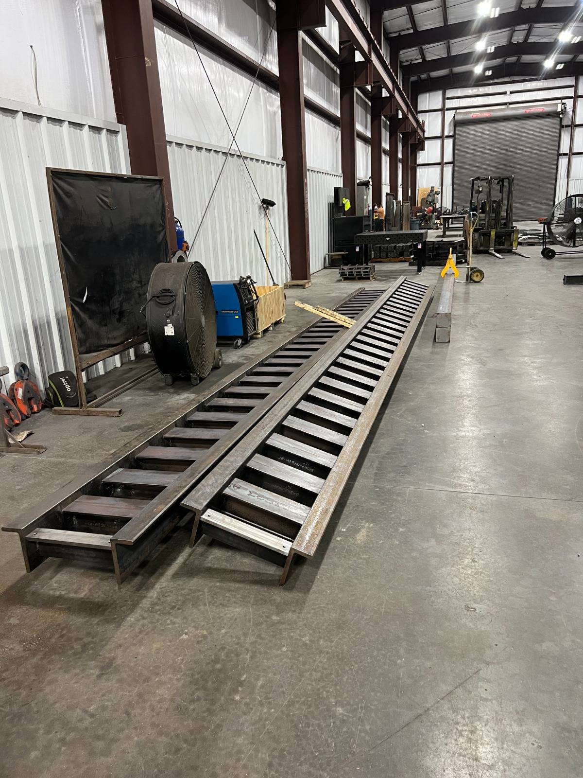 Two long fabricated rails lying on the concrete floor of the fabrication shop