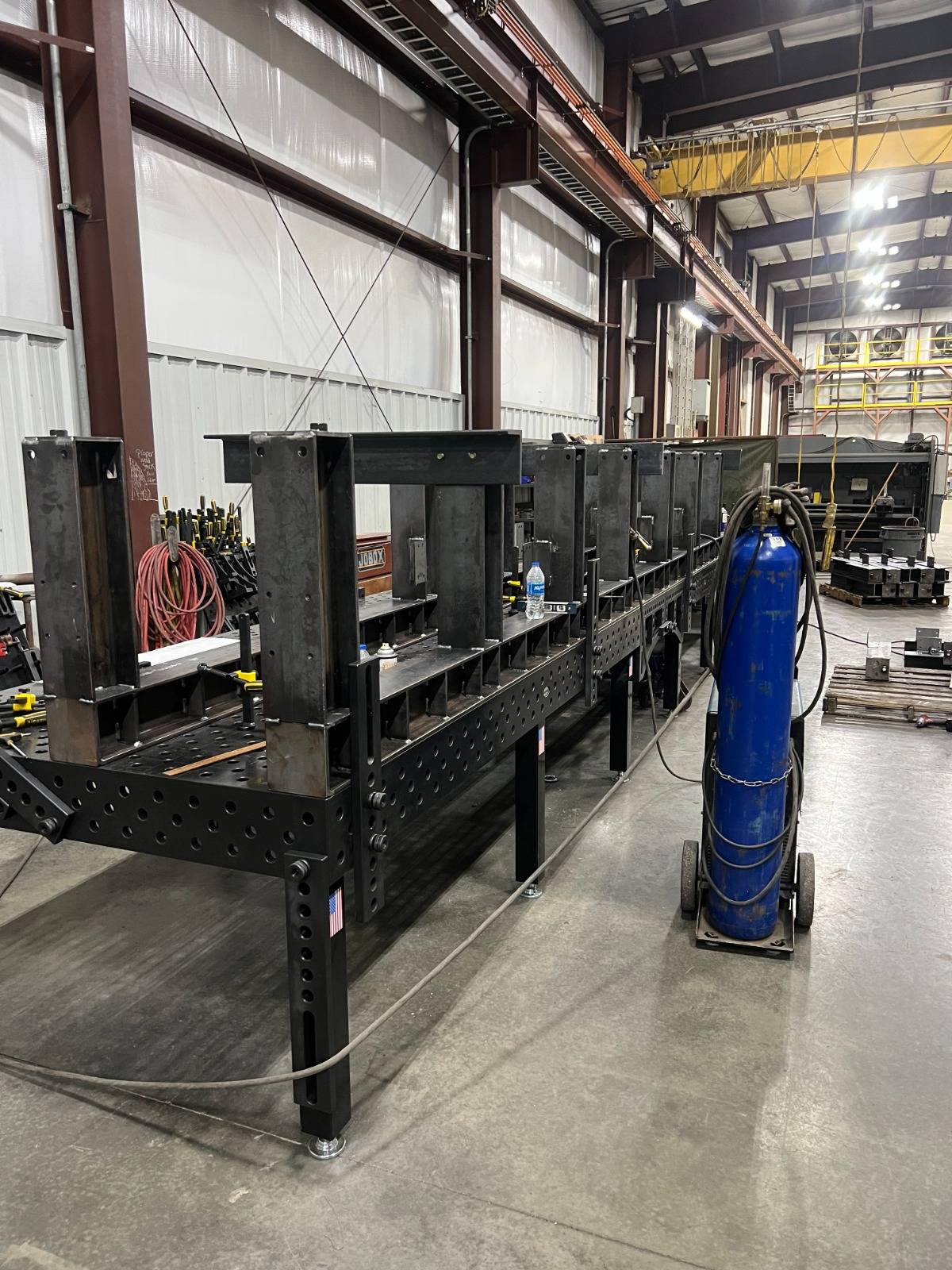 Long structural weldment on stands inside the Pierce fabrication shop, with an overhead crane above