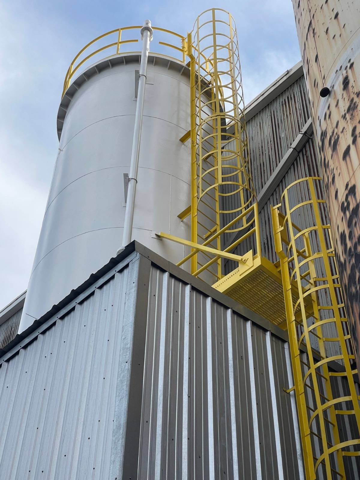 Yellow safety cage and ladder installed beside an industrial tank
