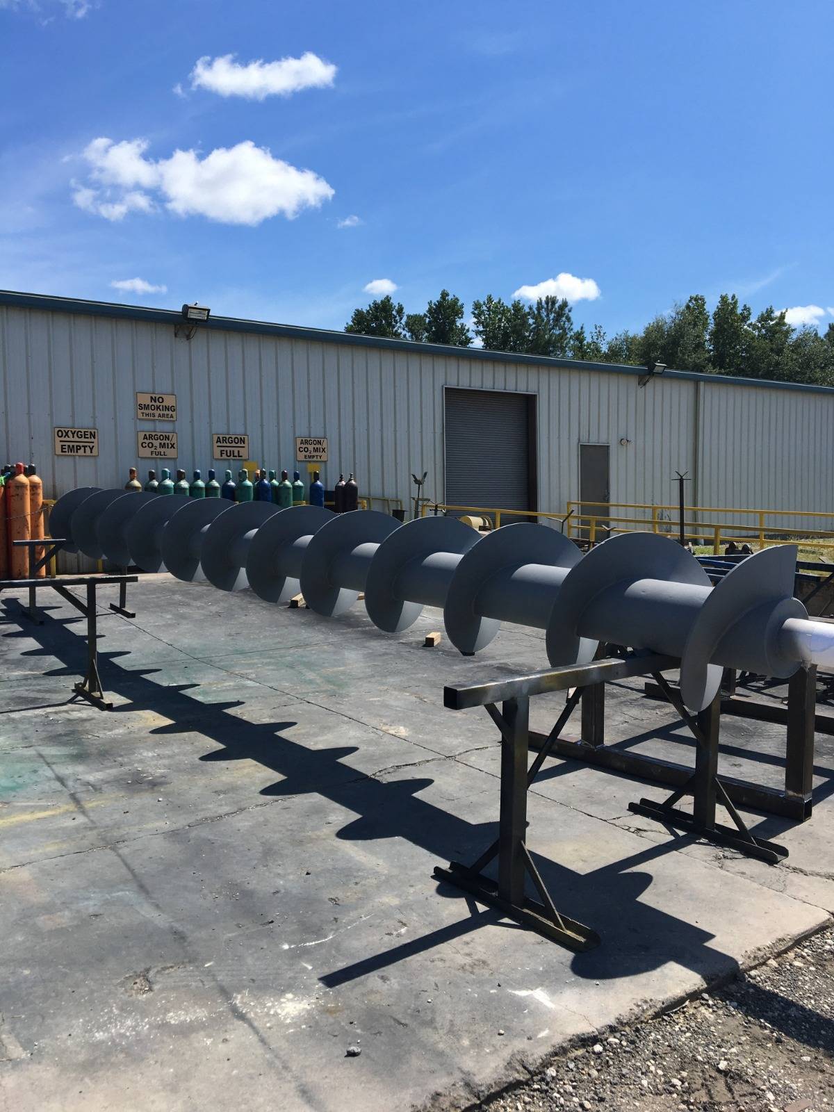 A long screw conveyor staged on stands outside the shop